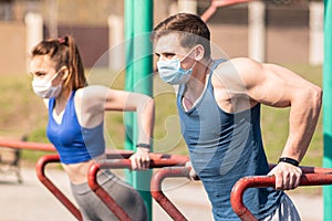 A young guy and a girl push up on the bars in medical masks during a pandemic