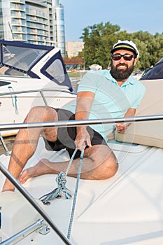 A young guy in glasses is sitting on a yacht pulling a winch