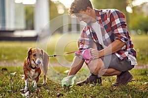 A young guy is in a good mood while collecting the poop of his dog in the park. Friendship, walk, pets