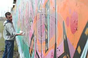 A young guy in a gray hoodie paints graffiti in pink and green c