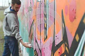 A young guy in a gray hoodie paints graffiti in pink and green c