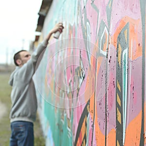 A young guy in a gray hoodie paints graffiti in pink and green c