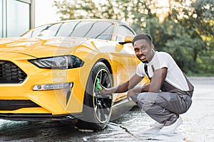 Young guy in gray overalls African bearded man cleaning a wheel, car rims