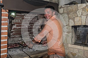 Young guy grills meat in a fireplace on an open fire