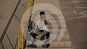 Young guy is happy about new news, sitting on the urban stairs, talking on smartphone.