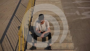 Young guy is happy about new news, sitting on the urban stairs, talking on smartphone.