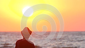 Young guy in a hat watching the sunset by the ocean. The male traveler enjoys the view of the east and the waves. Silhouette of a