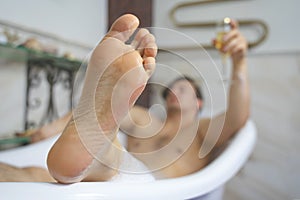 Young guy having a foam bath relaxing. Drinking champagne. Focus on the leg