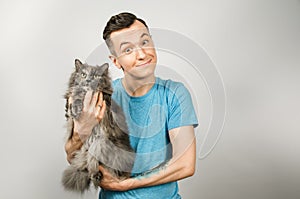 Young guy holds gray Britain cat on light gray background