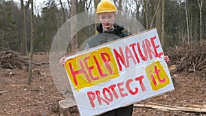 A young guy holds poster help nature protect it, in forest.