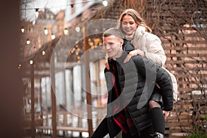 Young guy laughs and carries a beautiful girl on his back. Yellow bokeh in the background. Valentine`s day concept