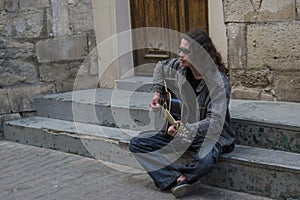 Young guy with long hair in sunglesses playing guitar on the street