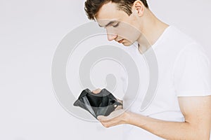 A young guy looks in an empty wallet. Isolated white background