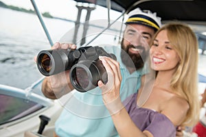 A young guy looks with a girl in binoculars on a yacht