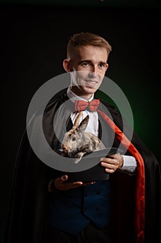 A young guy magician illusionist holding a hat with a rabbit