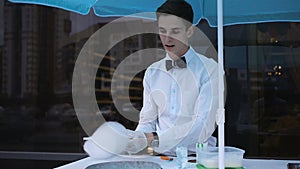 Young guy making cotton candy on a special machine, it wears bow tie, behind him balloons