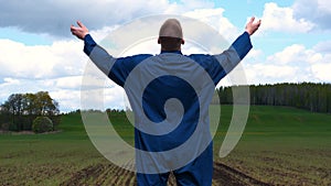 A young guy man, a farmer in a working uniform, walks across a field in rubber boots. Concept of: Freedom, Rubber boots, Lifesty