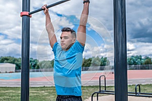 Young guy, man sports athlete, in summer in city on sports ground, pulls up on bar, workout fitness, workout healthy