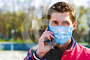 Young guy in medical mask talking on mobile phone in park