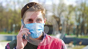 Young guy in medical mask talking on mobile phone in park
