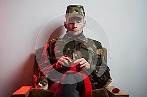 A young guy in a military uniform sits in a chair and knits in a quiet environment