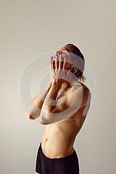 Young guy with muscular, fit, sportive shirtless body standing in underwear against grey studio background