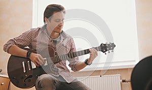 Young guy musician composes music on the guitar and plays in the kitchen, close up