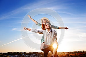 Young guy piggybacking cheerful girlfriend like airplane on the background of sky