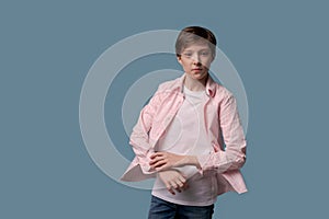 Young guy in pink shirt and white t-shirt poses in studio on a blue background.