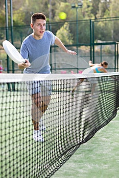 Young guy playing padel tennis on open court in summer