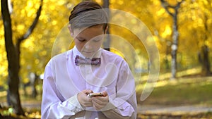 Young guy playing in the phone and walking in the autumn park.