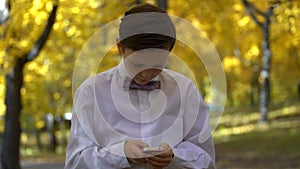 Young guy playing in the phone and walking in the autumn park.