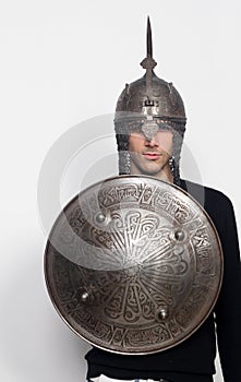 Young guy is posing in studio with helmet and shield. Knight, halloween concept.