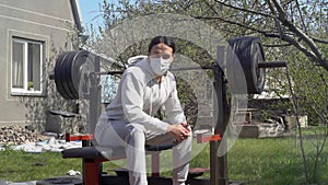 A young guy, in a protective mask, during quarantine rests after traning in the garden