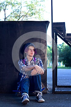 A young guy with purple hair sits on a skateboard in the park on the asphalt