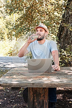 A young guy quenches thirst, drinks water from a bottle while sitting at a table in the park