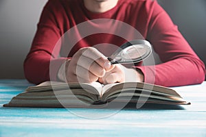 A young guy reading a book with a magnifying glass