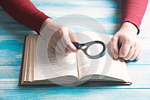 A young guy reading a book with a magnifying glass