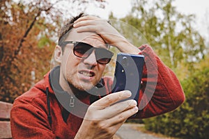 Young guy reads news or SMS on a mobile phone and holds his head with his hand. disappointment of the message on the