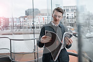 A young guy reads a newspaper inside.