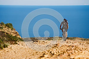 A young guy riding a mountain bike on a bicycle route in Spain on road against the background of the Mediterranean Sea