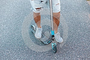Young guy riding a scooter. Men`s feet in denim ripped stylish shorts in white sneakers. Close-up