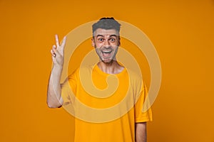 Young guy screaming with joy and showing peace sign isolated over yellow wall