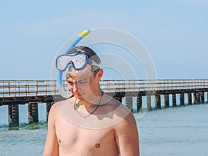 A young guy with a scuba mask and a snorkel near the pier for mooring.