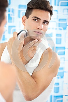 Young guy shaving his beard off with an electric shaver