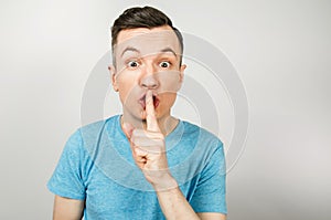 Young guy shut your mouth with finger dressed in a blue t shirt on a light background