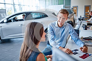 A young guy signing documents in the showroom to buy a new car.