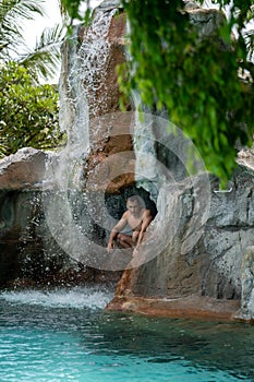 A young guy sits in a rock behind a waterfall