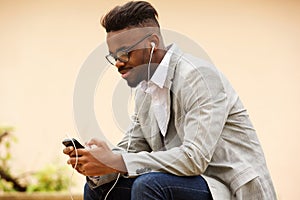 Young guy sitting outside listening to music with mobile phone