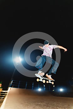 Young guy skateboarder doing a jump trick at night in a skatepark